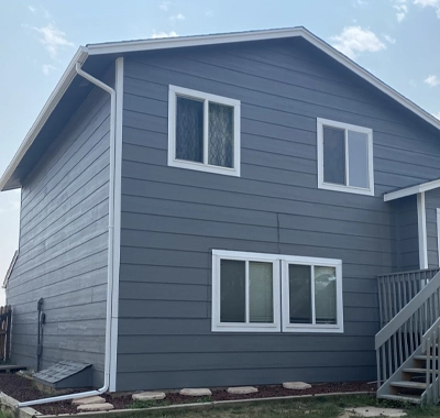 Gray house exterior with two levels and white-framed windows.