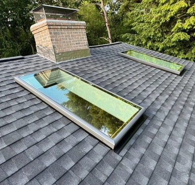 Skylight windows on a gray shingled roof with a brick chimney.
