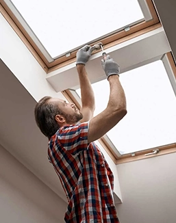 Man installing a skylight window wearing gloves in a checkered shirt.