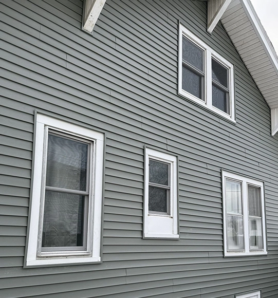 Grey siding on a house exterior with multiple white-framed windows.